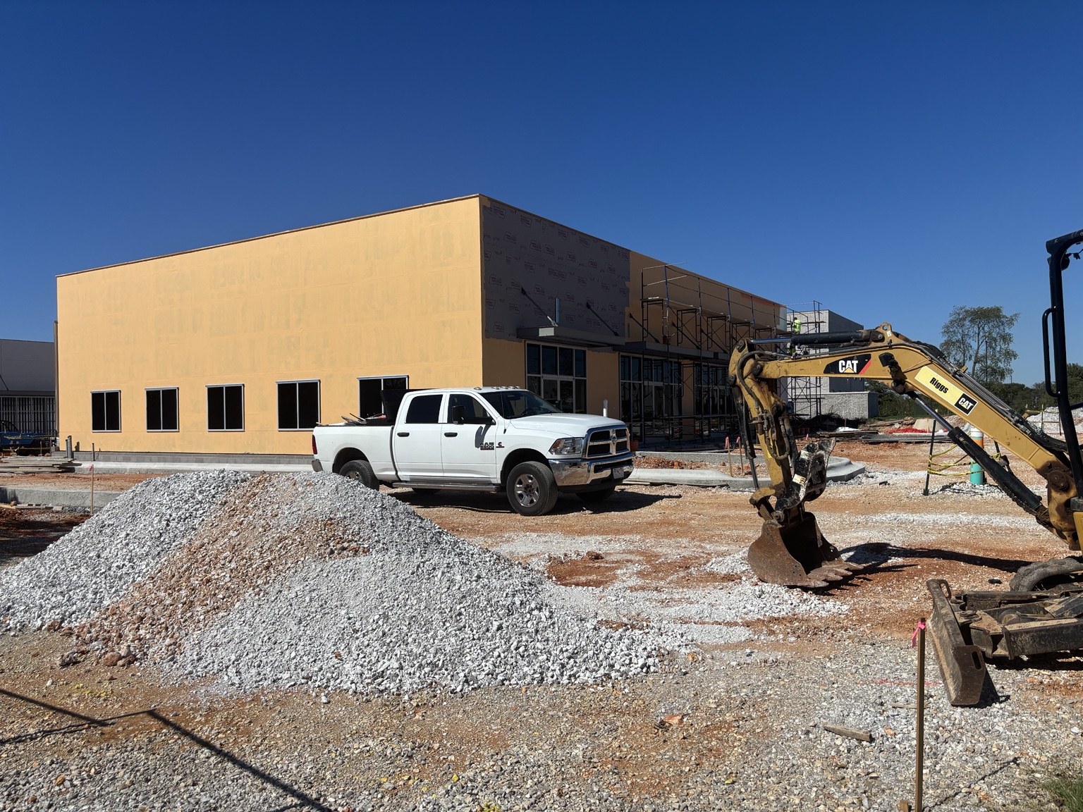 Commercial lease building under construction at the NABOR property, with window openings, storefront framing, scaffolding, a pickup truck and an excavator.
